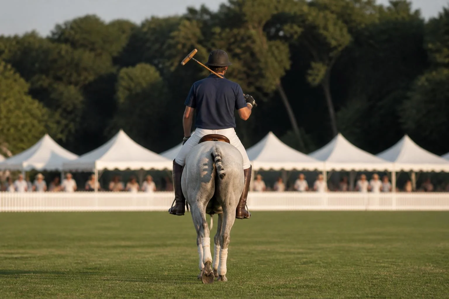Joueur de polo vu de dos au pas sur un poney gris bandé, maillet sur l'épaule, tentes blanches et forêt derrière