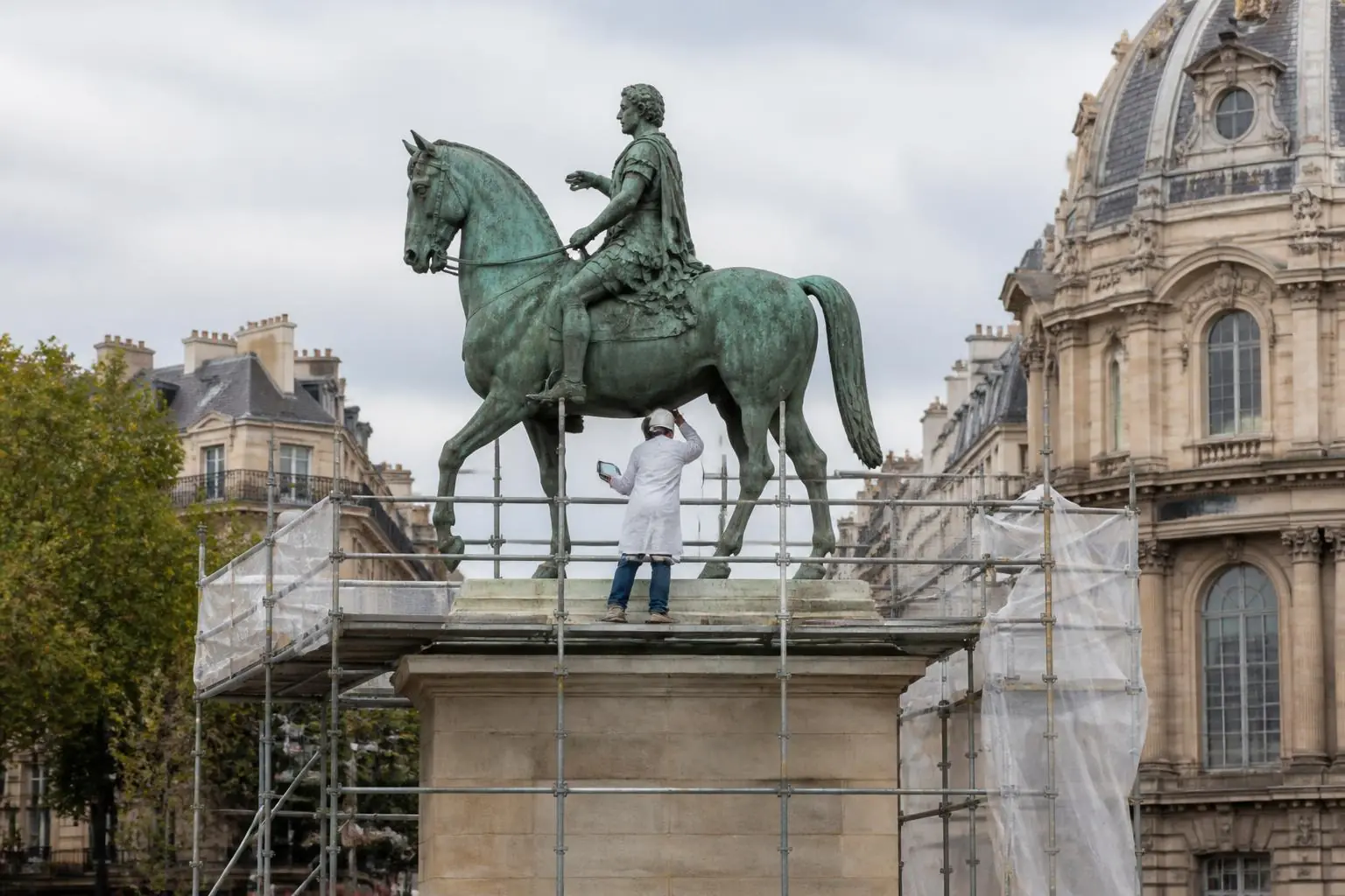 Un restaurateur en blouse blanche, sur un échafaudage, inspecte une statue équestre en bronze à la patine verte