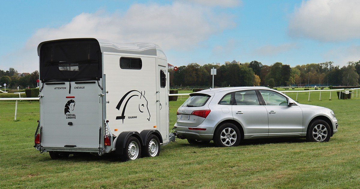 Van Cheval Liberte Touring Jumping blanc attele a un SUV sur un terrain herbeux de concours