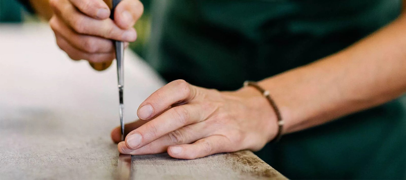 Mains d'un sellier Devoucoux tracant sur une piece de cuir a l'atelier