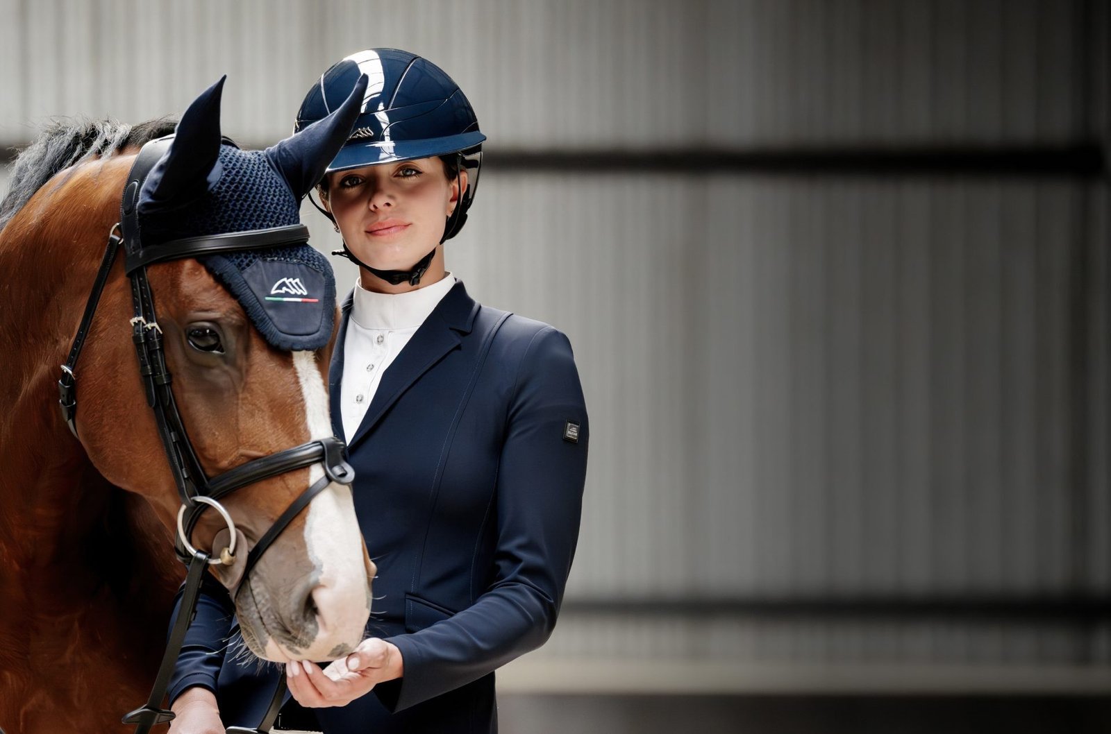 Cavaliere en veste bleu marine coiffee d'un casque Equiline Xanto bleu, tenant son cheval bai equipe d'un