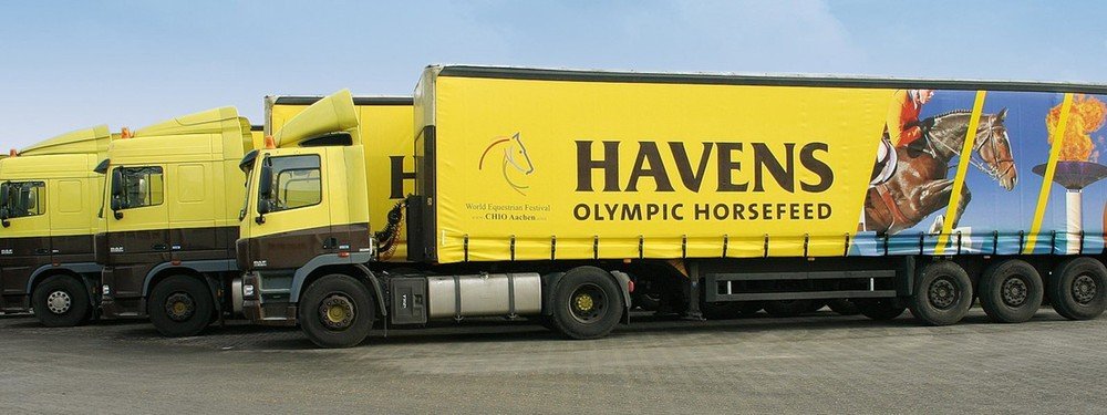 Camions jaunes Havens Olympic Horsefeed alignés, remorque décorée d'un cheval à l'obstacle