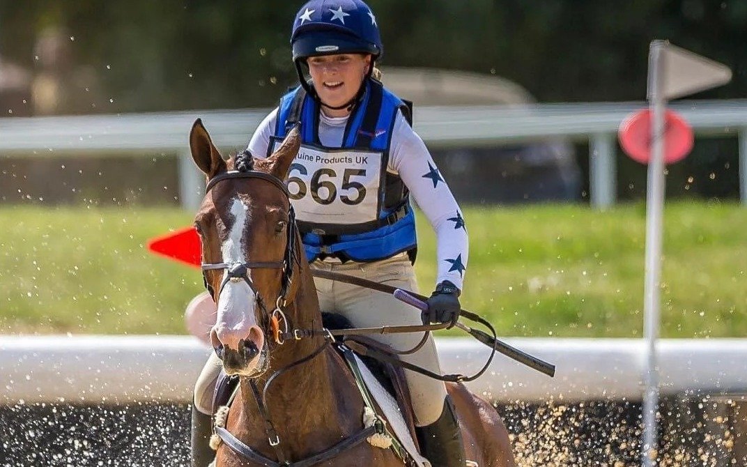 Cavalière de cross au passage d'un gué, gilet airbag Point Two bleu roi à logo rouge