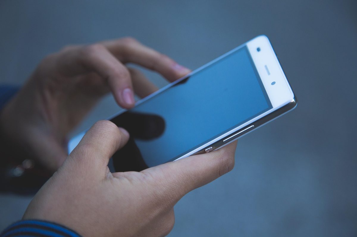 Main tenant un smartphone pour consulter les cotes et placer un pari hippique en ligne sur un site agréé ANJ